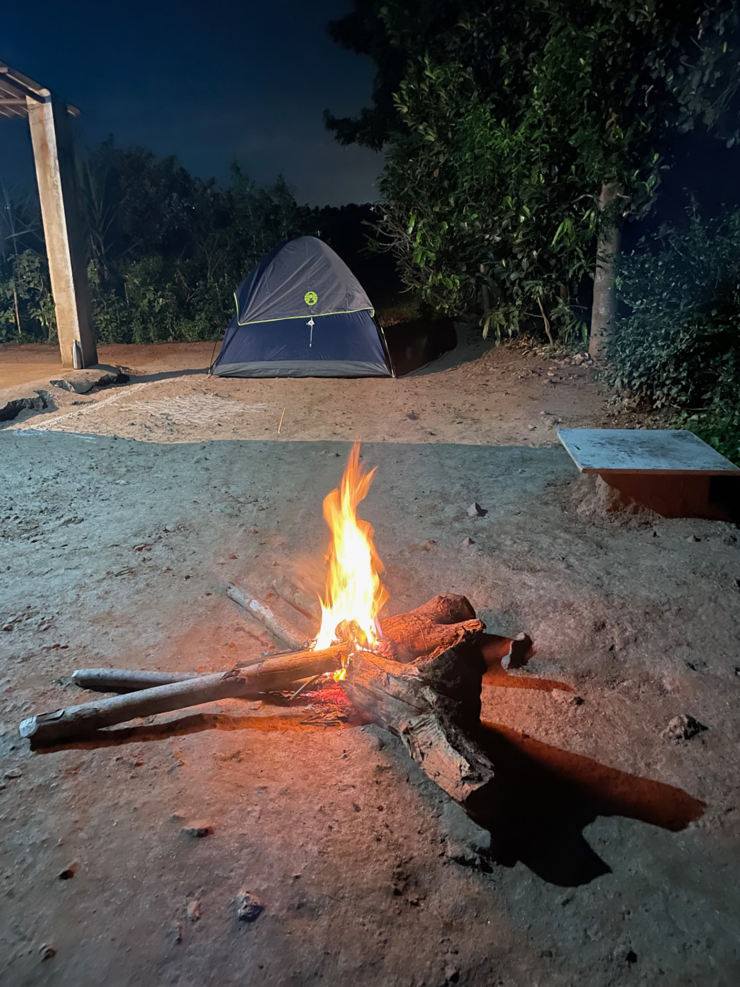 Campfire burning beside a tent pitched at the farm at night